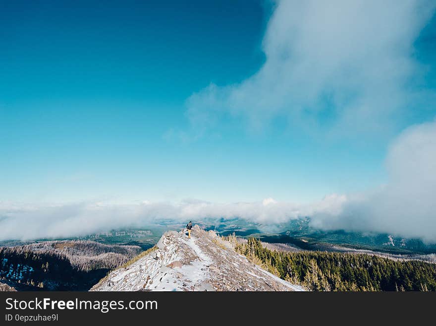 Hiker standing on snow capped mountain summit against blue skies on sunny day. Hiker standing on snow capped mountain summit against blue skies on sunny day.