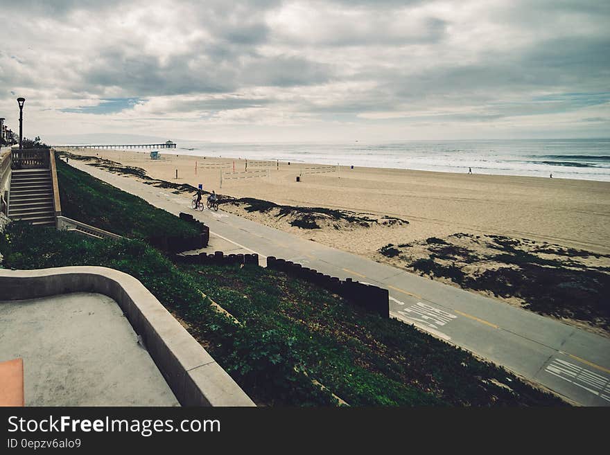 Road along sandy beach shoreline with cloudy skies.