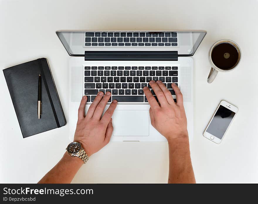 Overhead view of hands of worker typing on laptop with notebook, mobile and cup of coffee, white background. Overhead view of hands of worker typing on laptop with notebook, mobile and cup of coffee, white background.