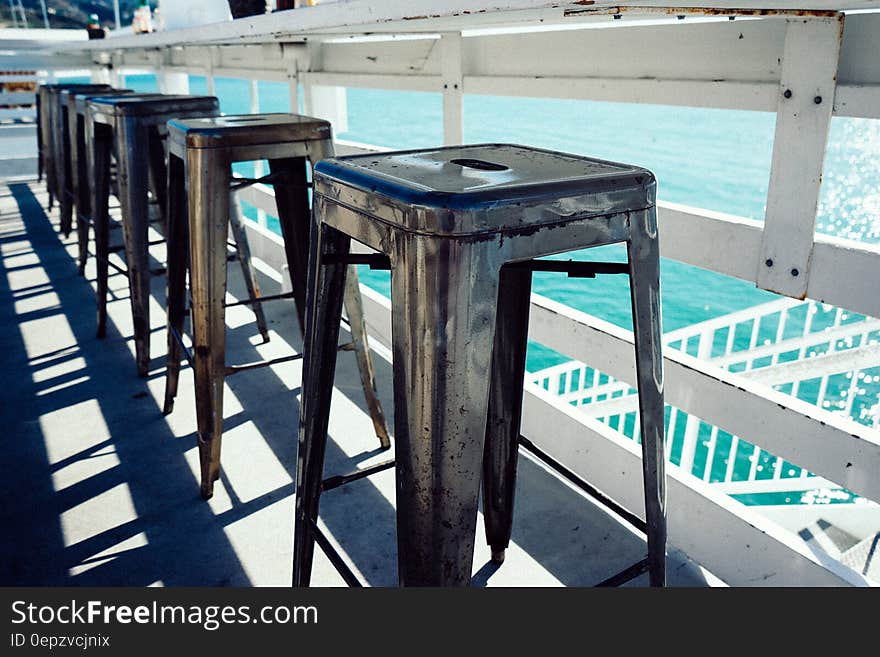 Row of wooden stools on outdoors balcony overlooking water. Row of wooden stools on outdoors balcony overlooking water.