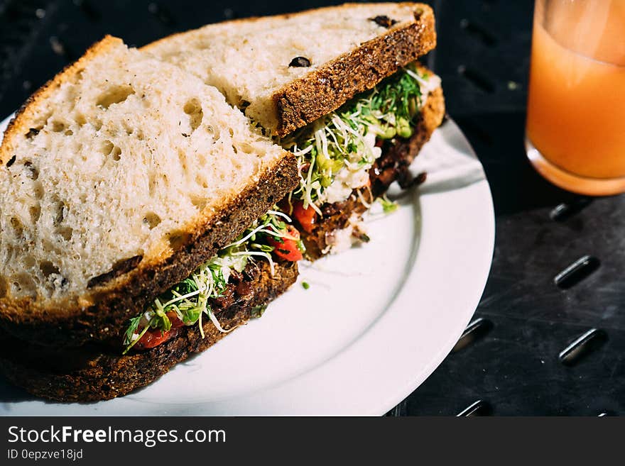 Fresh salad sandwiches on plate with drink of orange juice.