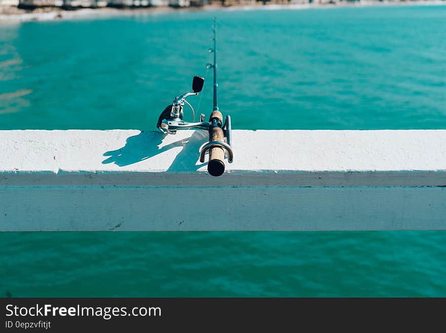 Fishing rod and reel on white fence overhanging sea. Fishing rod and reel on white fence overhanging sea.