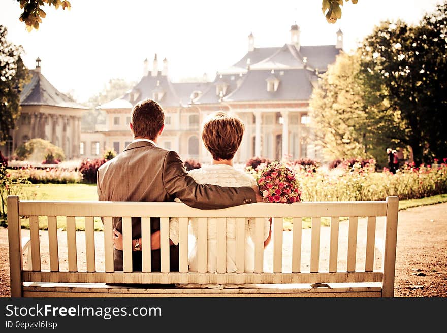 Wedding couple sitting together on a bench looking at a stylish mansion in front of them. Wedding couple sitting together on a bench looking at a stylish mansion in front of them.