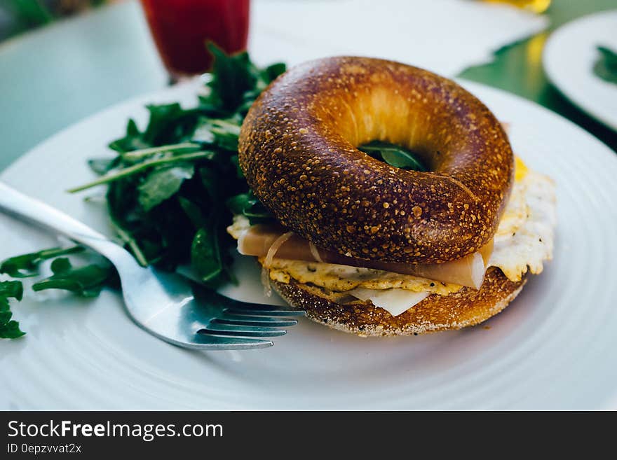 A bagel sandwich with fried egg and cheese and salad beside on a plate.