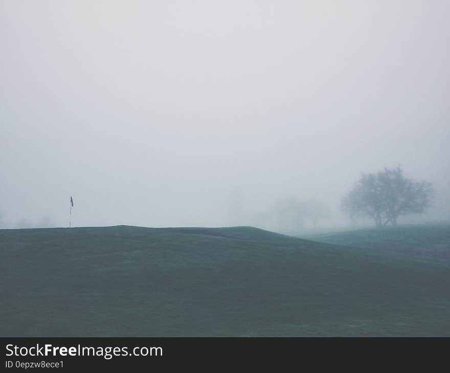 Mist covering golf course with flag in foreground.