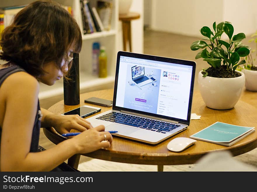 Woman in Black Tank Shirt Facing a Black Laptop Computer on Brown Wooden Round Table
