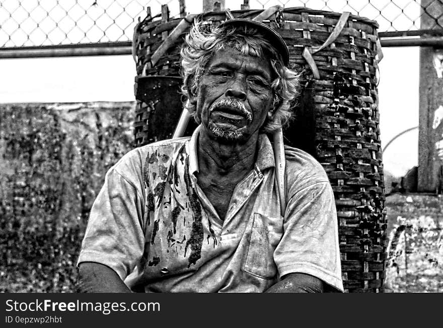 Man in Polo Shirt Sitting Near Brown Woven Basket Black and White Photography