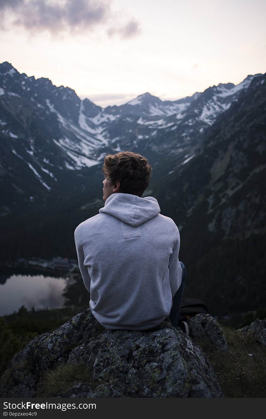 Man Wearing White Hoodie Sitting on a Rock With a View on Mountain