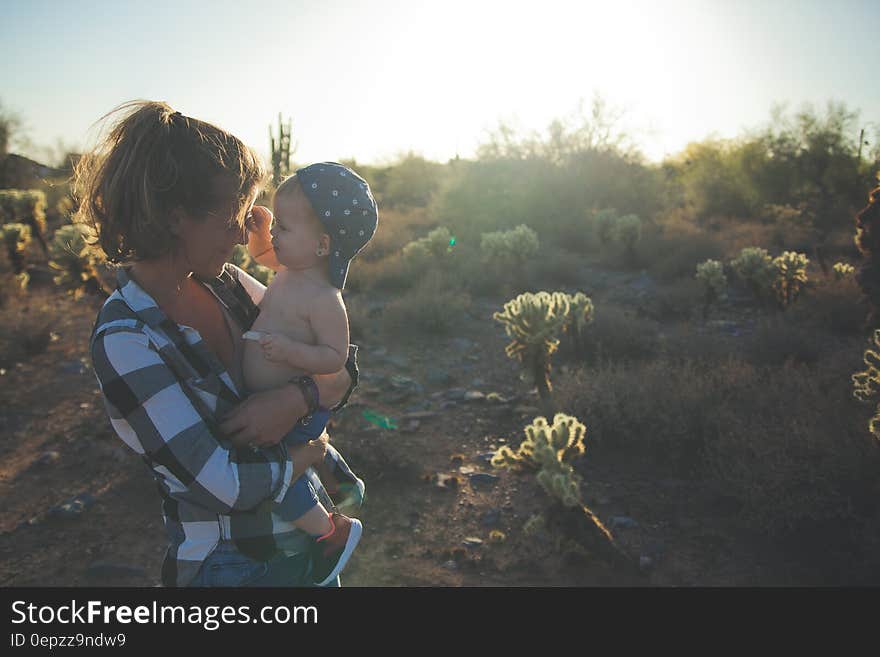 Woman in White Black and Grey Checkered Dress Shirt Carrying Baby With Blue Cap