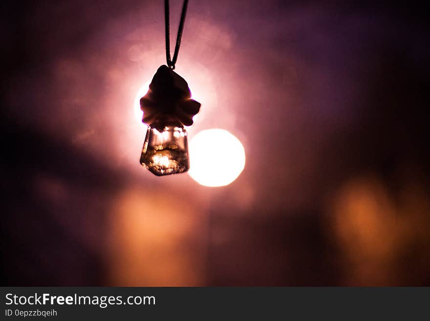 Silhouette of car freshener hanging against bokeh lights.