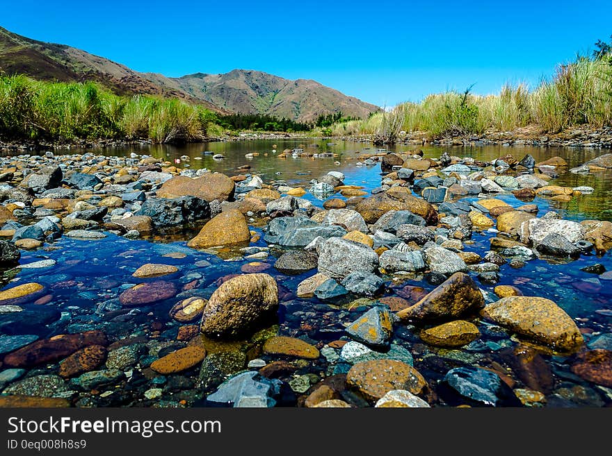 Stones at edge of picturesque lake with mountains and blue sky background.