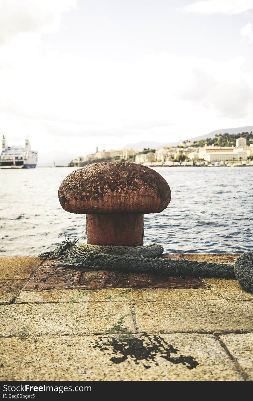 Old rope and mooring on dock with sea and large boat in background.