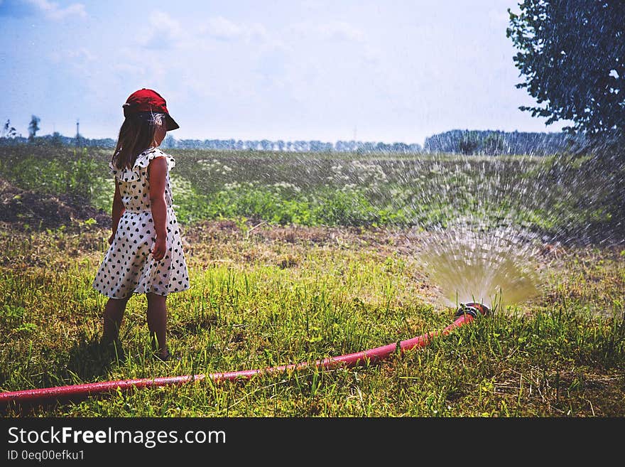 Girl on Green Grass Near Red Hose While Pumping Water during Daytime