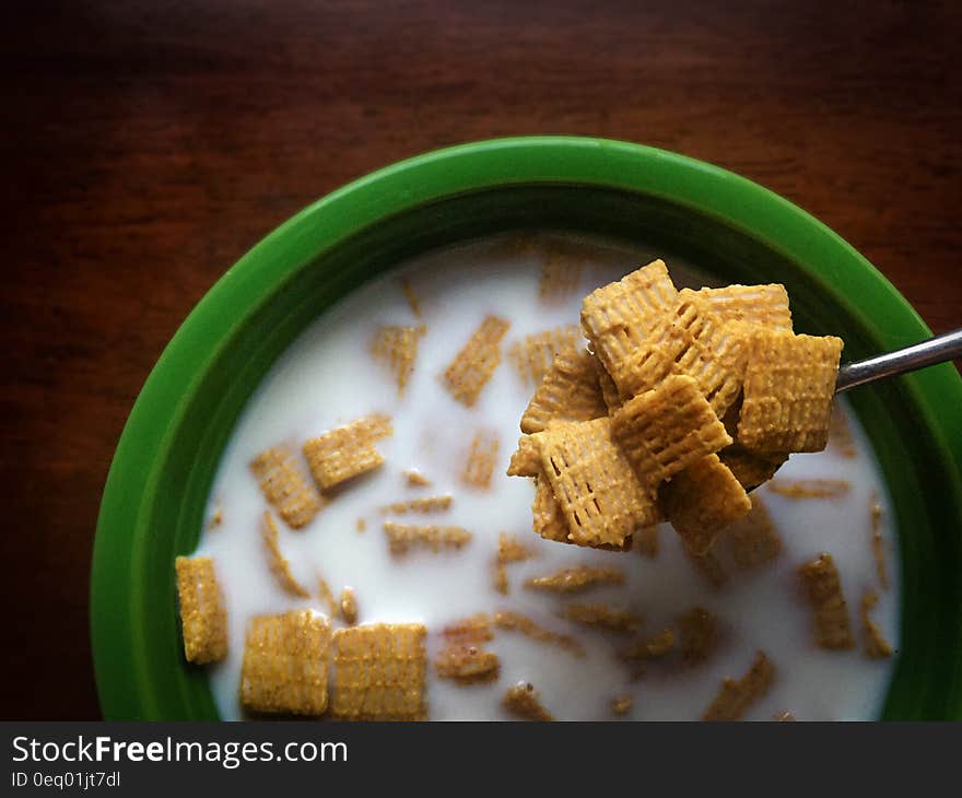 Overhead view of breakfast cereal on spoon over green bowl with milk.