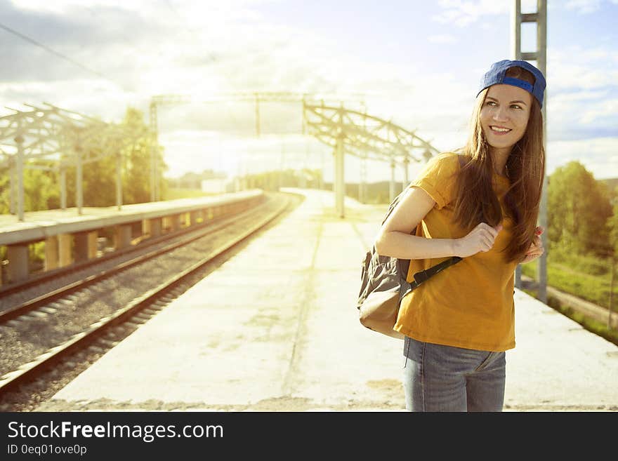 Smiling Woman in Orange T Shirt and Blue Snap Back Cap Carrying Backpack