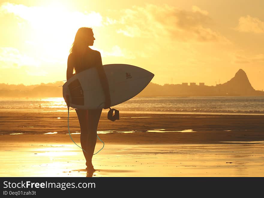 Woman Holding Surf Board Standing on Shoreline during Sunset