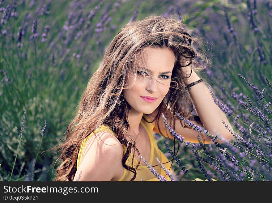 Women&#x27;s Yellow Tank Top Holding Her Brown Curly Hair While Sitting on a Purple Flower