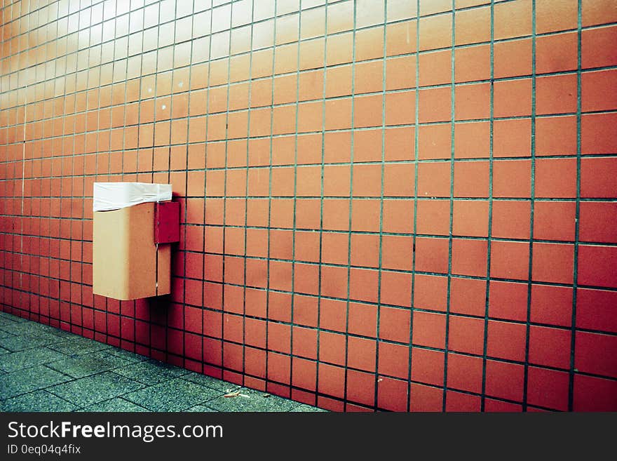 Trash can mounted on wall with orange tiles by floor with green tiles. Trash can mounted on wall with orange tiles by floor with green tiles.