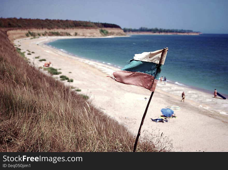 Blue Ocean Near on White Sands With White Blue and Red Flag on Shore