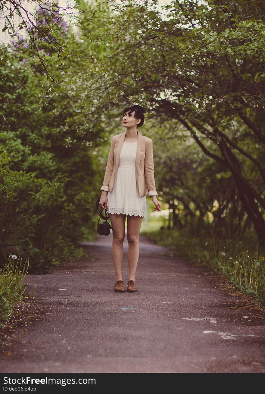 Woman in Beige Blazer Standing on Pathway Surrounded by Green Trees during Daytime