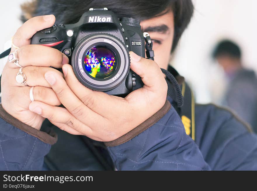 Young man in blue jacket taking a picture with a Nikon single lens reflex digital camera. He is composing the picture and focusing while viewing the scene through the eye piece. Young man in blue jacket taking a picture with a Nikon single lens reflex digital camera. He is composing the picture and focusing while viewing the scene through the eye piece.