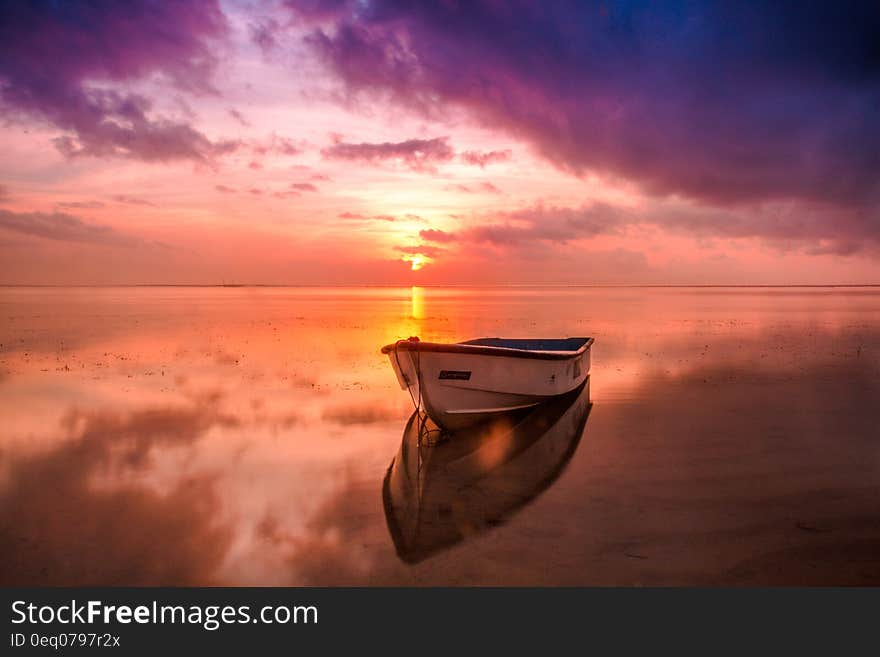 Small boat anchored in a bay on a tranquil sea colored by a magical sunrise of orange, yellow, purple and brown. Small boat anchored in a bay on a tranquil sea colored by a magical sunrise of orange, yellow, purple and brown.