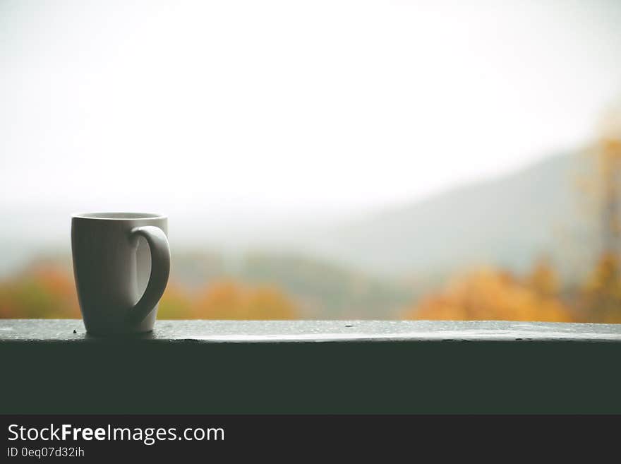 White Mug on Window over Looking Autumn Trees and Hills in Distance during Daytime