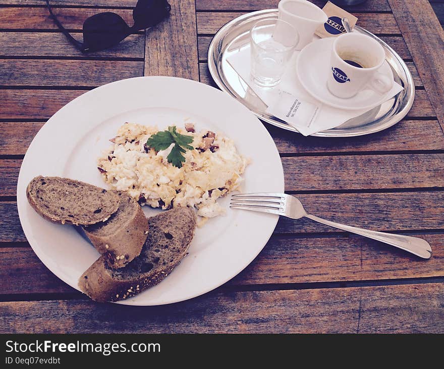 Stainless Steel Fork and White Ceramic Plate With Food on Top on Brown Wooden Table