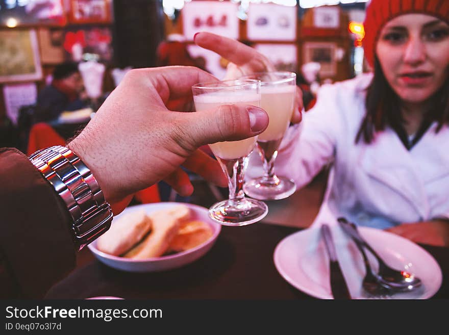 Man Wearing Silver Link Watch Holding a Glass Containing White Liquid in Front of a Woman