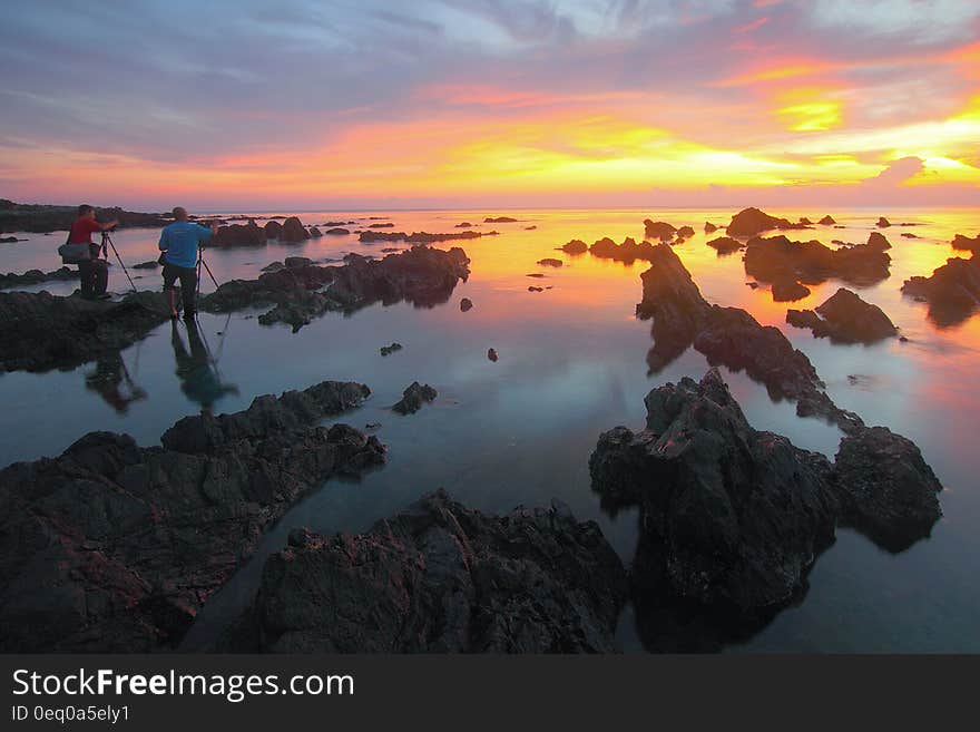 2 People Standing on Rock Formation Reflected on Water during Sunset