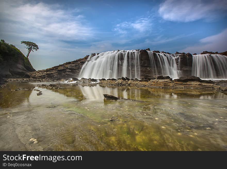 Waterfalls Near Hills Under Blue Sky and White Clouds