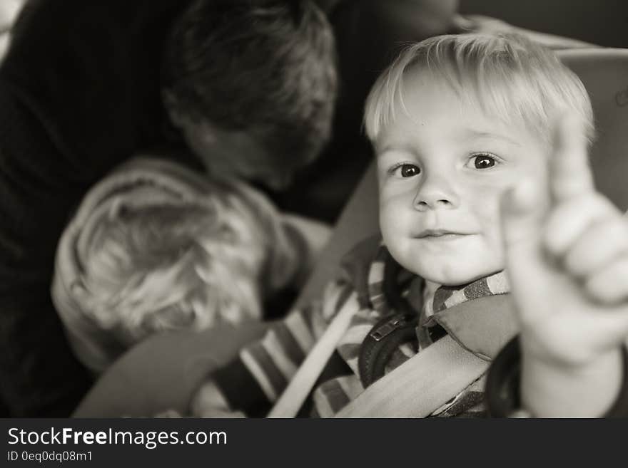 Black and white portrait of happy young boy pointing with brother and father in background.