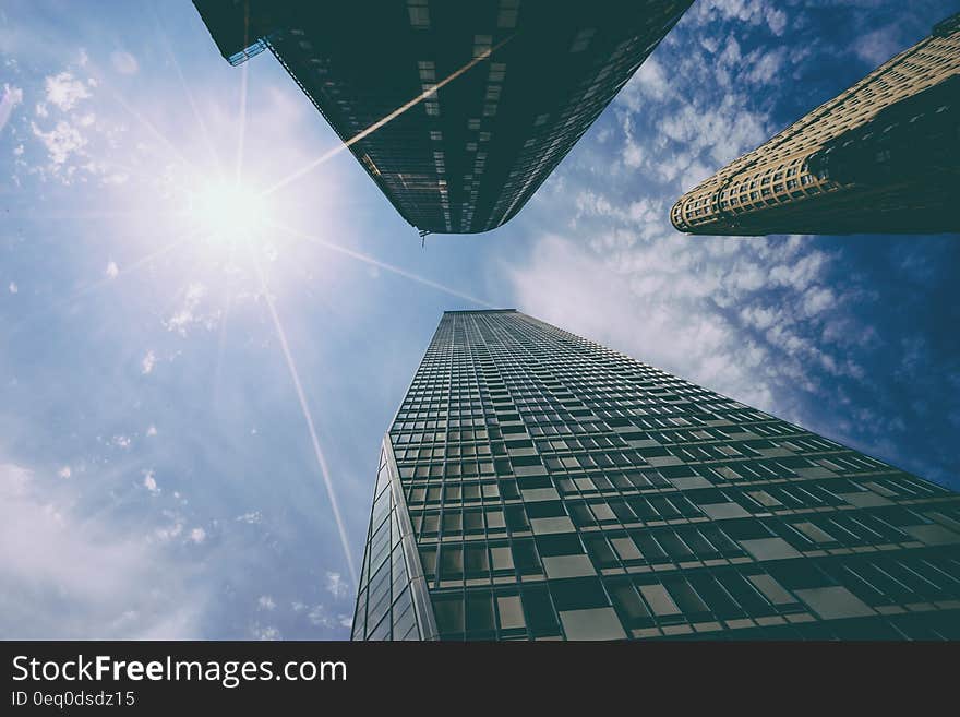 View looking up to top of three tall skyscrapers in city with cloudscape and sun flare. View looking up to top of three tall skyscrapers in city with cloudscape and sun flare.