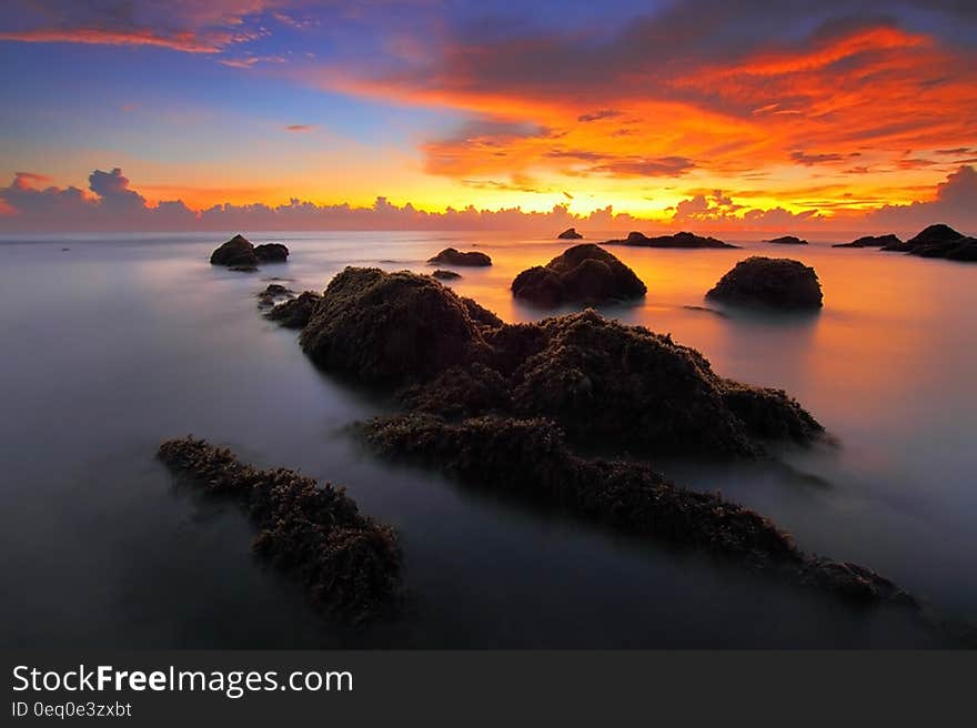 A sunset on the seashore with rocks rising from the water. A sunset on the seashore with rocks rising from the water.