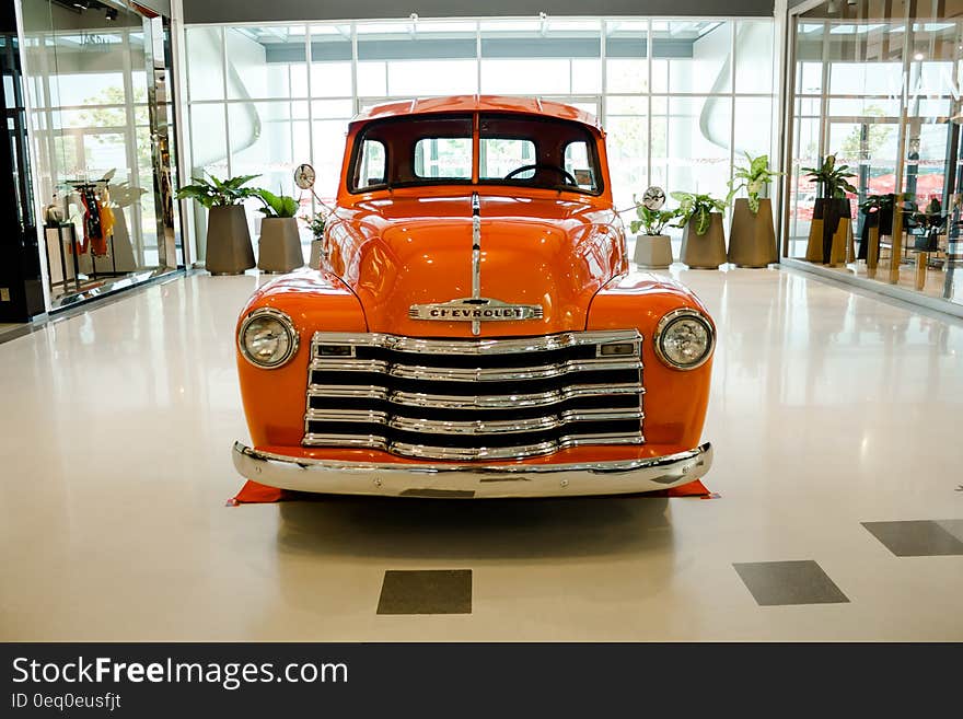 Orange colored Chevrolet sedan (saloon car) from 1950's in pristine condition with attractive chrome grill and headlights, pride of the garage and in the center of the showroom.