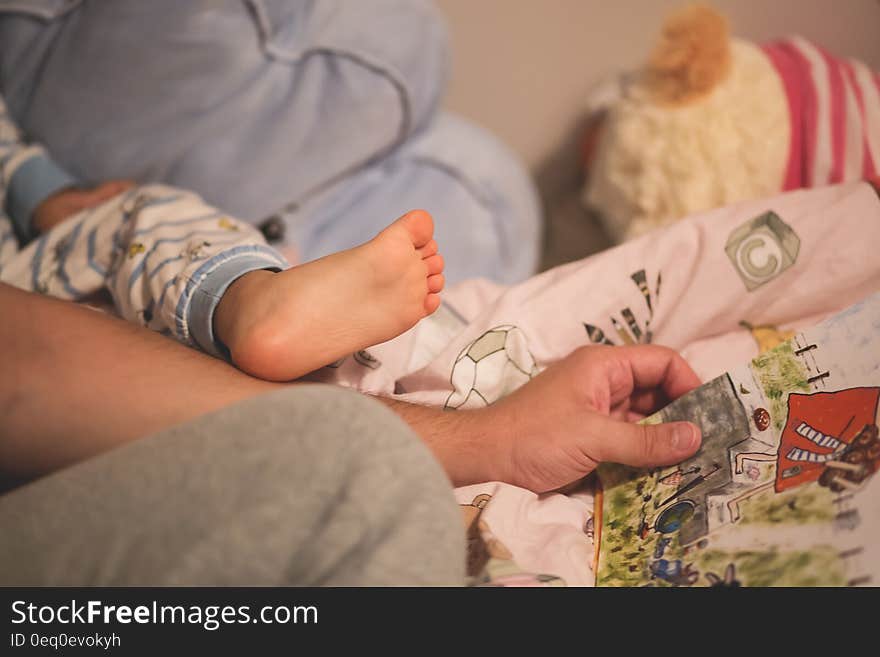 Small baby in bed showing a foot and pyjama leg and a parent's arm picking up a book maybe to read the child a bedtime story. Small baby in bed showing a foot and pyjama leg and a parent's arm picking up a book maybe to read the child a bedtime story.