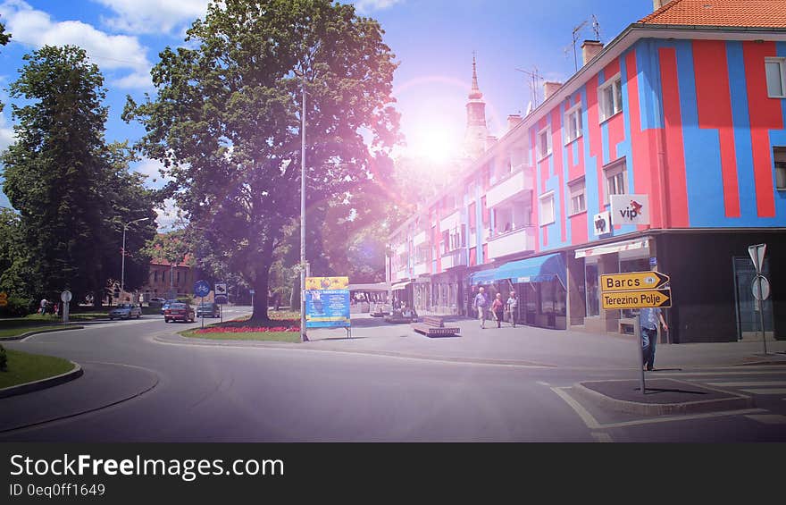 Unusual urban architecture with red and blue paneling in apartments above shops, orange tiled roofs and tree lined road.