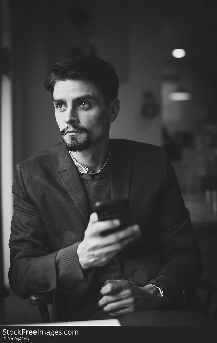 A black and white photo of a young businessman with a far off look holding smartphone. A black and white photo of a young businessman with a far off look holding smartphone.