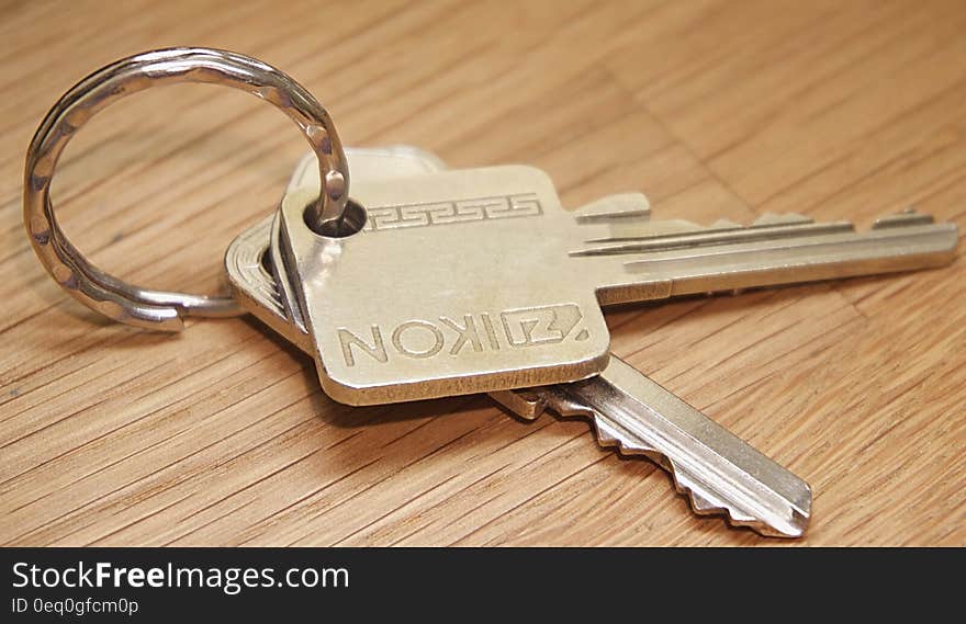 Closeup of two Yale style brass keys on a simple metal ring placed upon a grainy wooden table. Closeup of two Yale style brass keys on a simple metal ring placed upon a grainy wooden table.