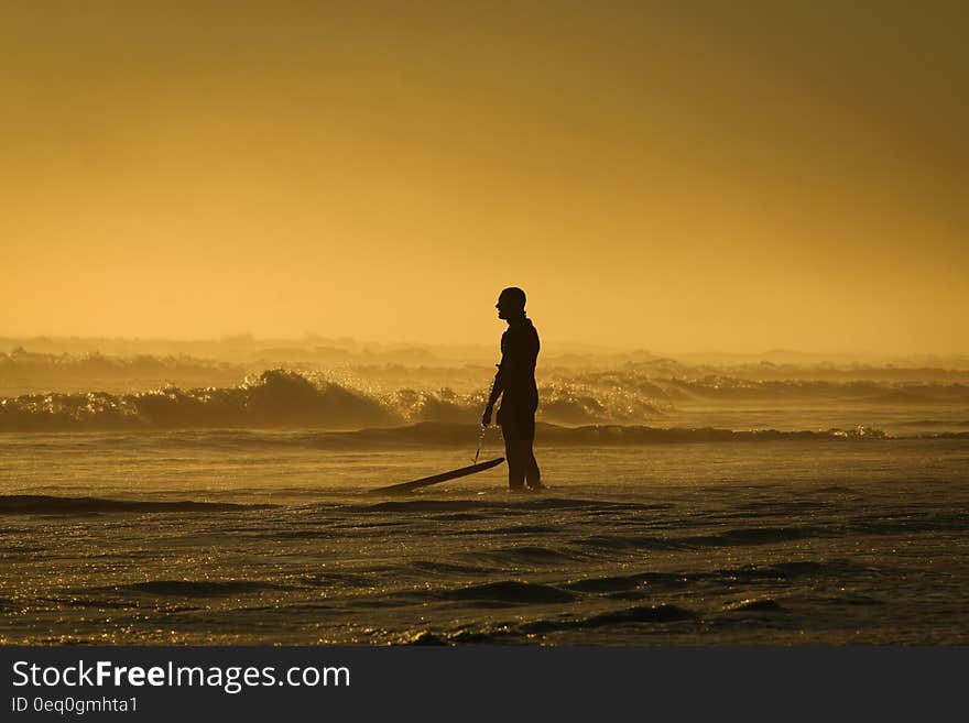 Man Standing on Seashore While Holding His Surfing Board during Sunset