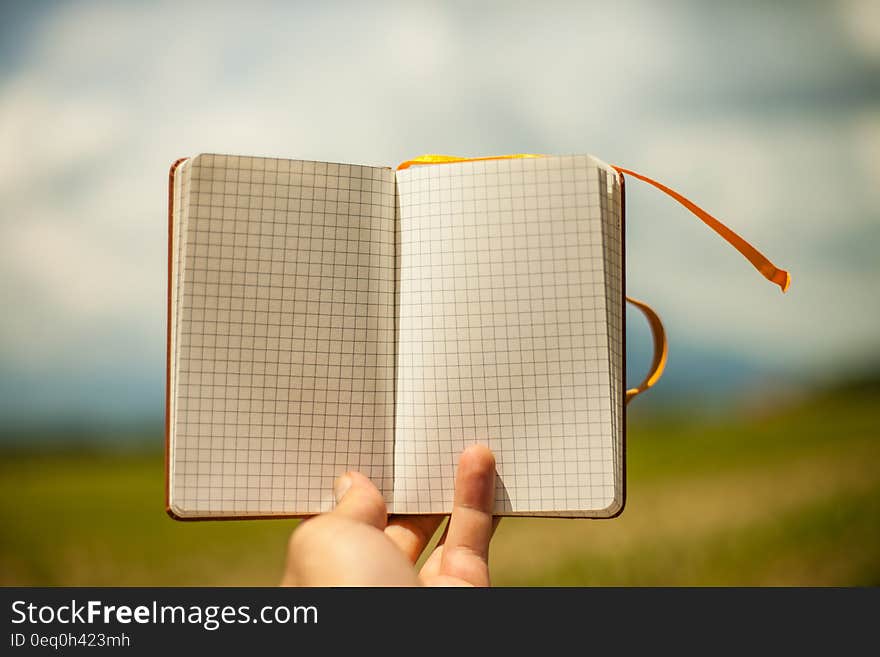 A close up of a hand holding an open blank notepad.