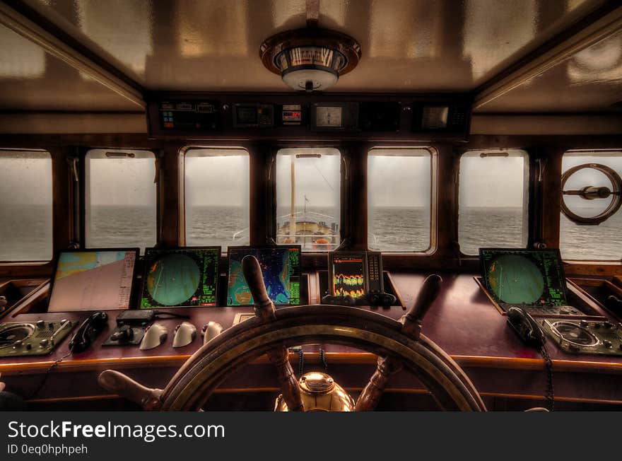 View from the wheelhouse of a older style ship across quiet sea to the horizon in darkening light with radar, navigation aids, telephone and wheel.