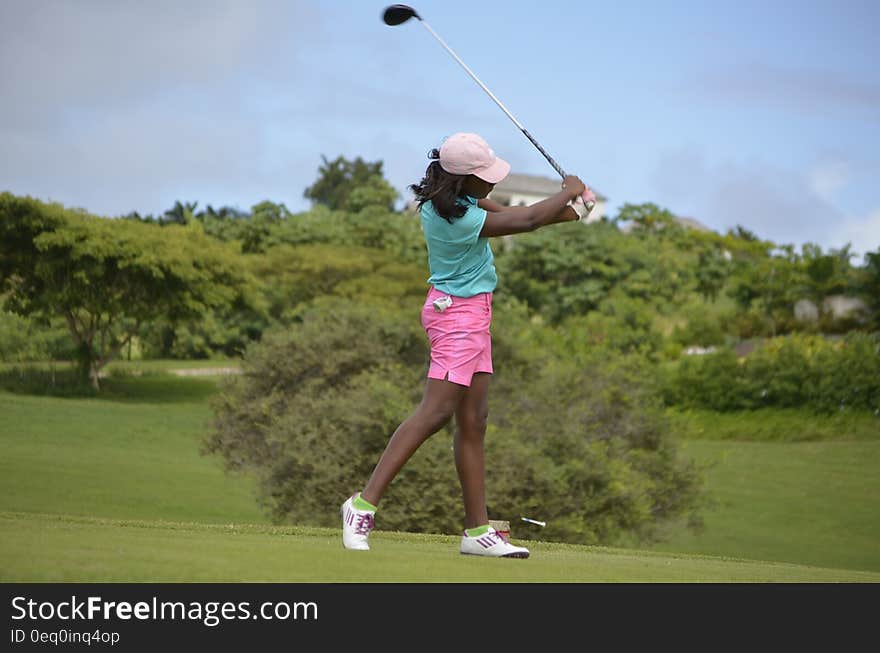 Woman in Green Polo Shirt and Pink Shorts Playing Golf Under Grey and Blue Skies during Daytime