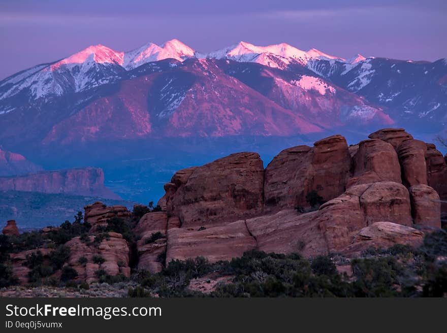 Green Trees and Rock Formation Overlooking Snow Coated Mountain Ranges at Daytime