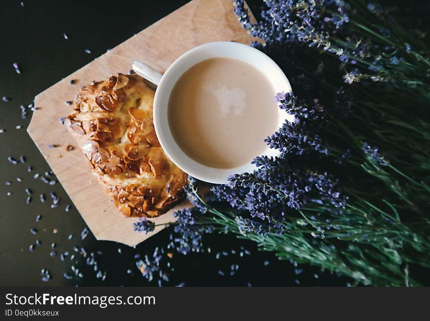 White Ceramic Mug With Brown Liquid Inside Beside Purple Flower and Pastry