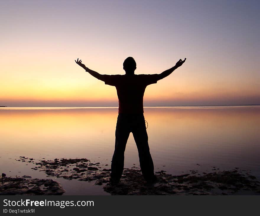 Silhouette of Man Standing Beside Ocean during Sunset