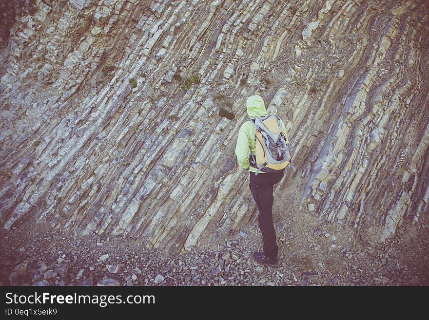 Person in Green Hoodie and Black Pants Walking Near Gray Rock