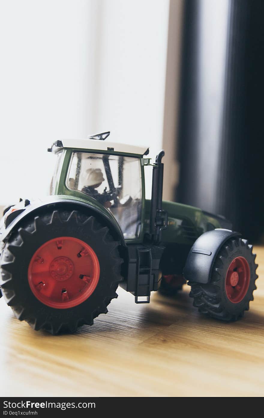 Black and Green Farm Tractor Toy on Brown Wooden Table Beside Window