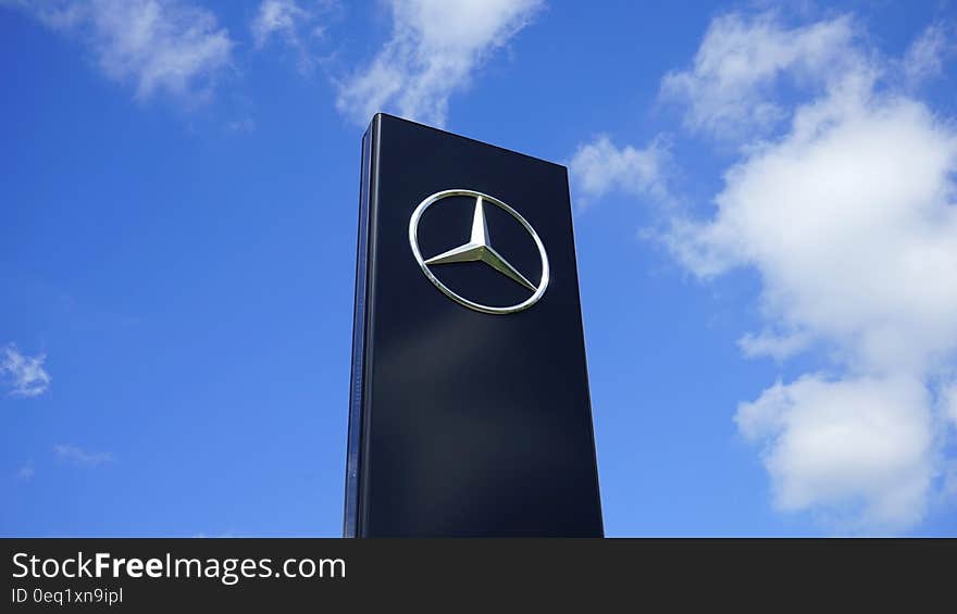 A Mercedes-Benz sign on a stand against the blue skies. A Mercedes-Benz sign on a stand against the blue skies.