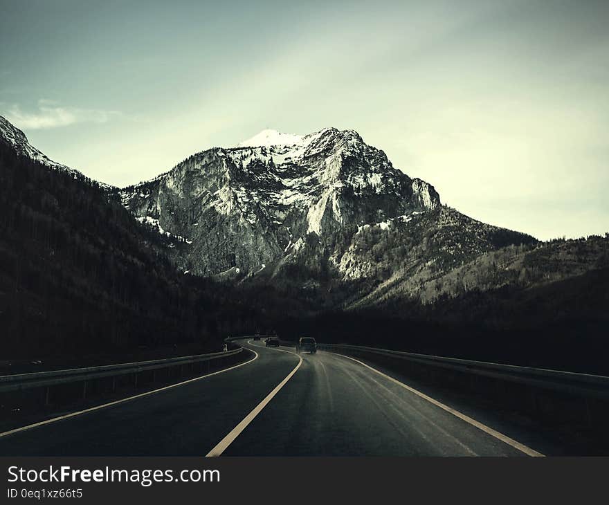 Asphalt Road With Running Vehicle Infront of Mountain Under Gray Sky